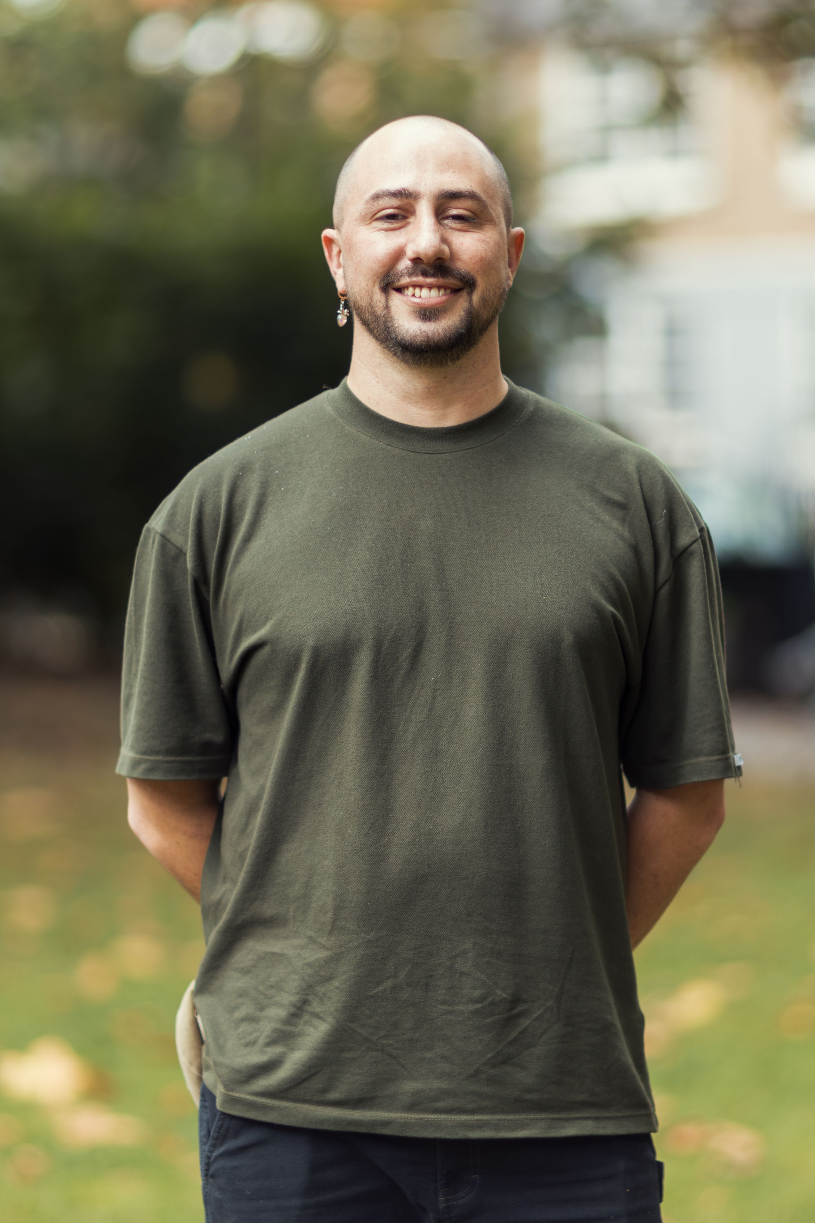 A man stands smiling in a green t-shirt in an outdoor park setting.