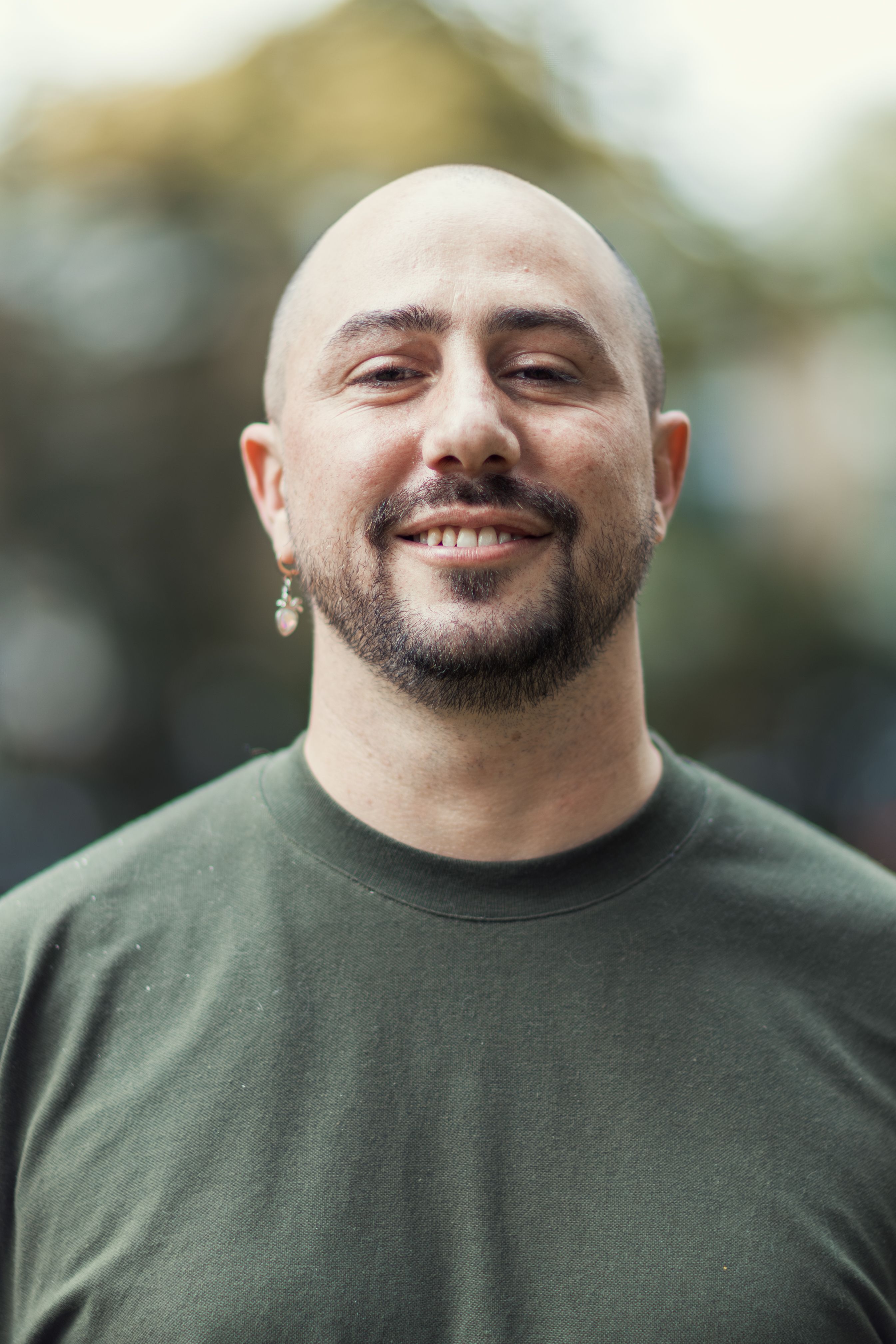 Portrait of a smiling bald man wearing a green shirt in an outdoor setting with a blurred background.