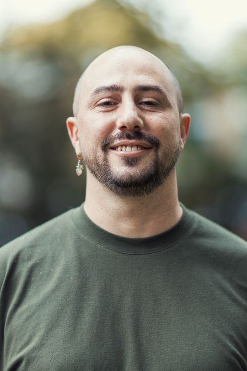Free Portrait of a smiling bald man wearing a green shirt in an outdoor setting with a blurred background. Stock Photo
