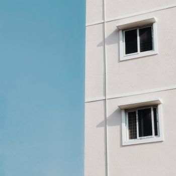 Simple building facade with windows contrasted against a clear blue sky, showcasing modernist minimalism.