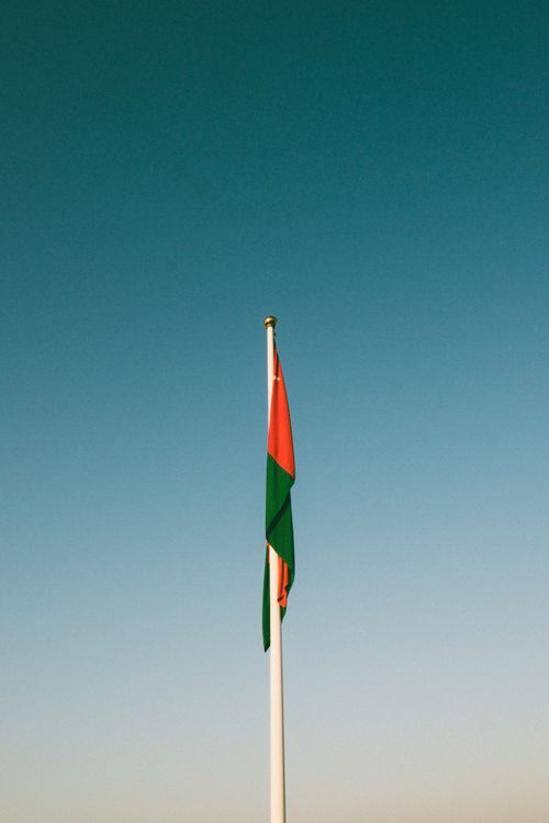 Free Omani flag waving on a pole against a clear blue sky in Muscat, Oman. Stock Photo