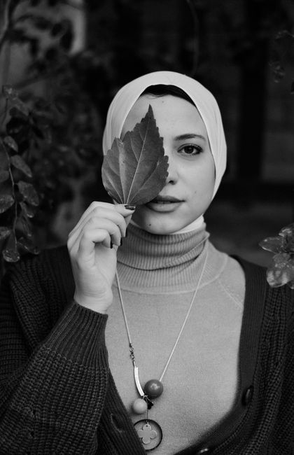 Stylish woman in black and white portrait hiding behind a leaf, showcasing elegance and beauty.