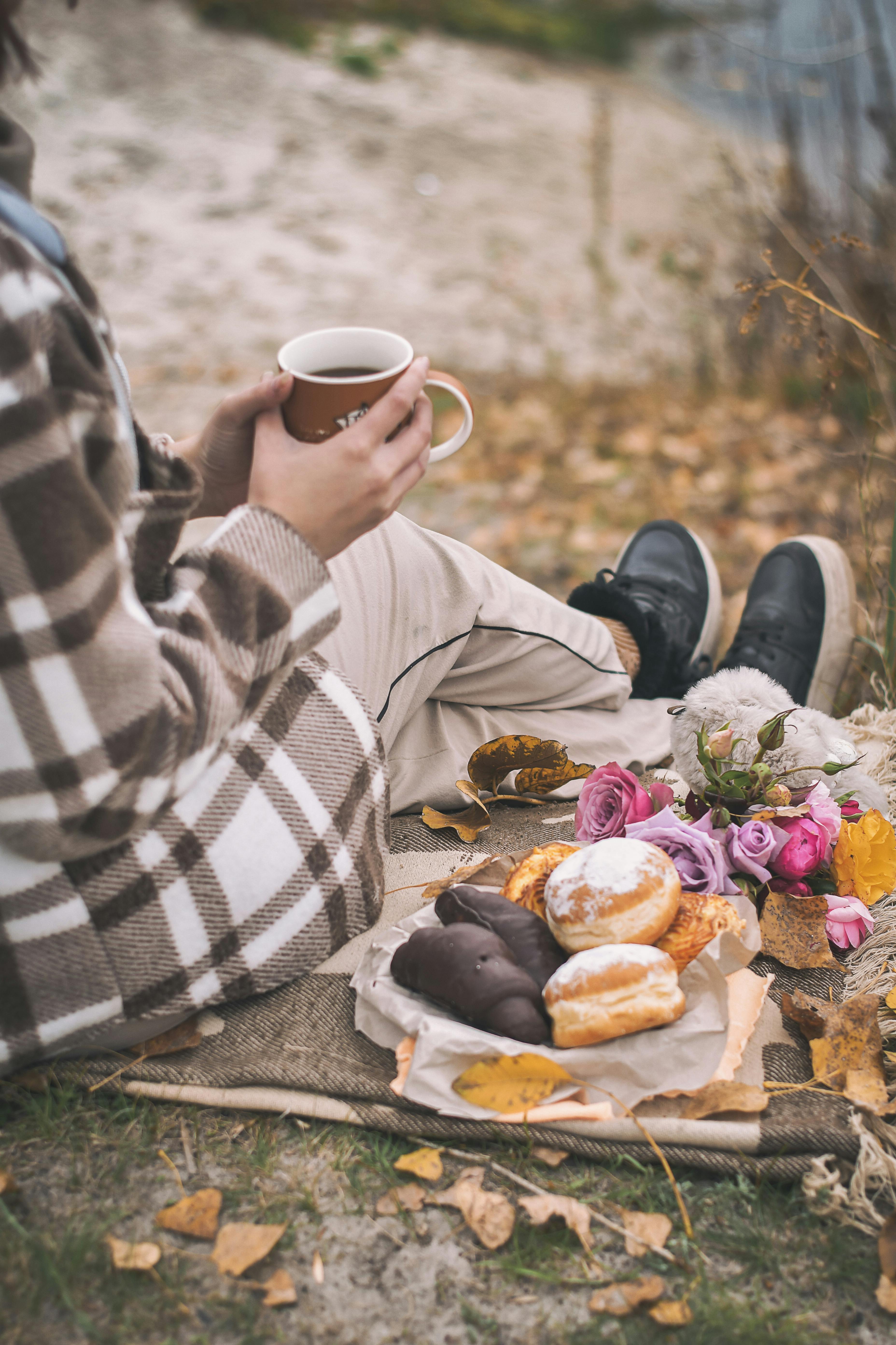 A warm autumn picnic featuring coffee, donuts, and flowers in a serene outdoor setting.