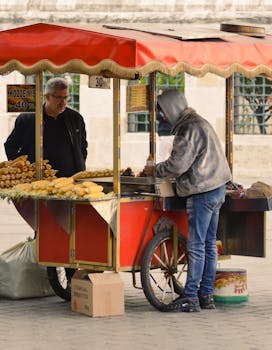A vibrant street market scene with a vendor selling grilled corn from a colorful red cart.