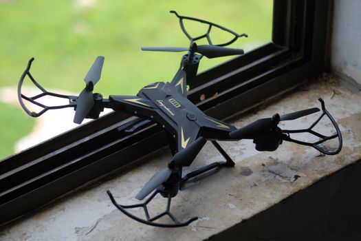 Black drone placed on window sill with greenery outside, offering a tech-lifestyle blend.