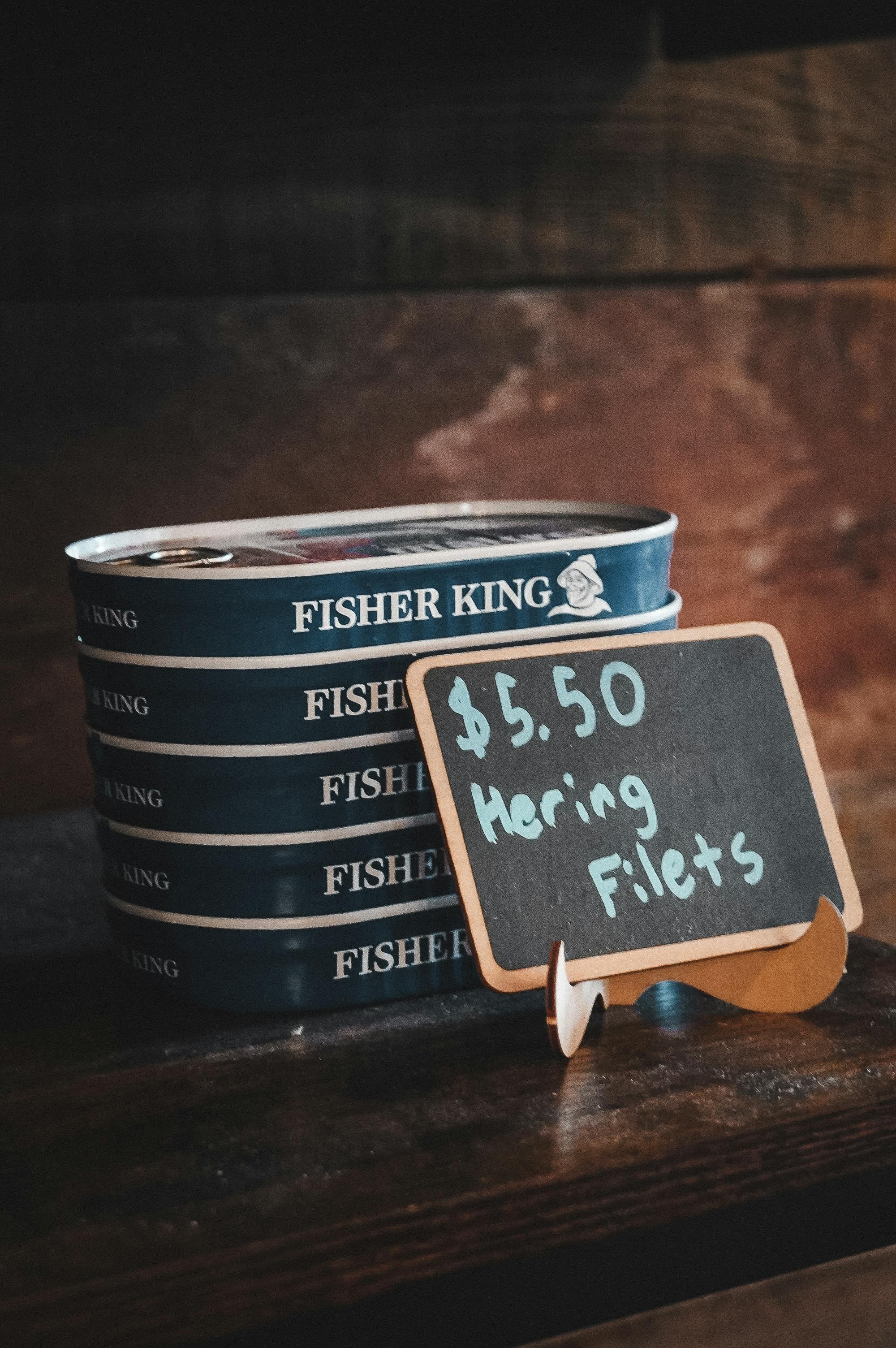 Stacked canned herring filets alongside a rustic chalkboard price display, conveying a vintage market vibe.