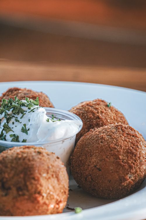 Free Appetizing plate of golden-brown croquettes with a side of creamy dipping sauce garnished with parsley. Stock Photo