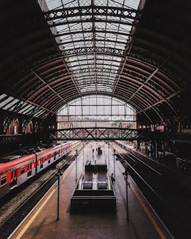 Image of a grand railway station with arched glass roof, showcasing trains and railway tracks.