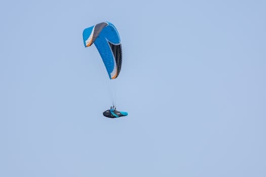 A lone paraglider flies high in a clear blue sky, showcasing adventure and freedom.