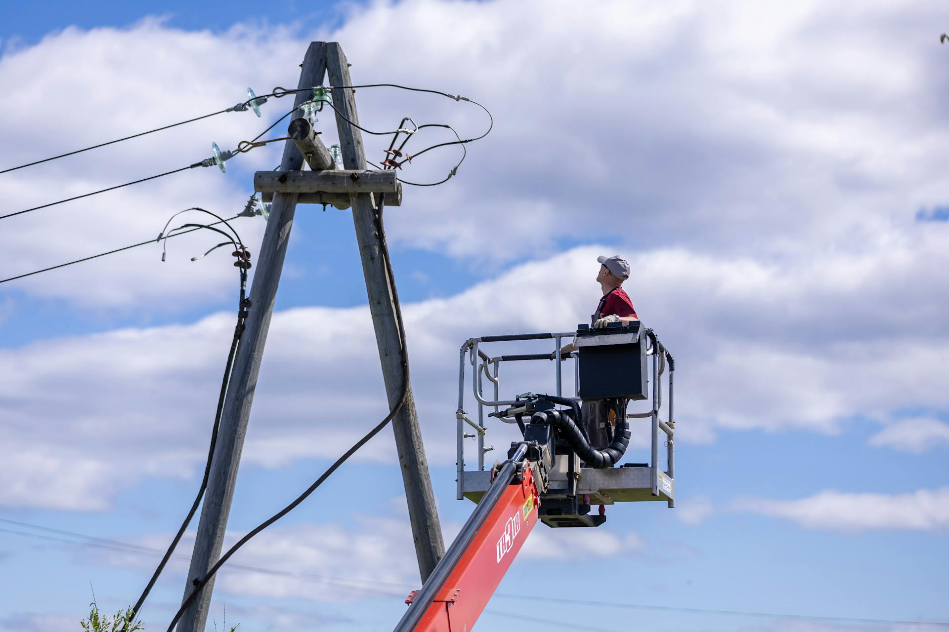 Worker on hydraulic lift repairing power lines on a clear day.