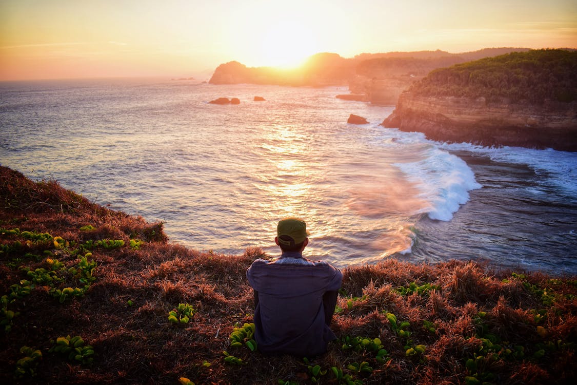 Free Man Sitting on Grass by the Cliff Stock Photo