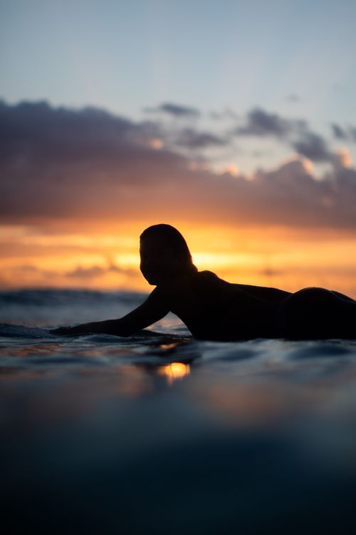Free A serene silhouette of a surfer paddling during a vibrant Hawaiian sunset. Stock Photo