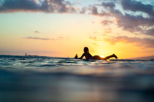 Silhouette of a surfer paddling during a vibrant Waikiki sunset in Hawaii.