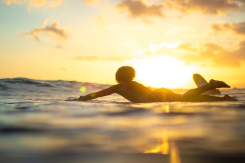 Free Surfer paddling through the golden sunset waves in Waikiki Beach, Hawaii, capturing the essence of island life. Stock Photo
