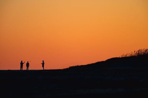 Free Silhouette of people engaging in play against a vibrant orange sunset, creating an evocative outdoor scene. Stock Photo