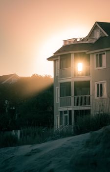 A serene sunset view behind a coastal beach house with balconies, casting soft light and shadows.