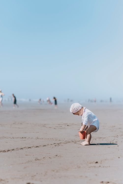 Free A toddler playing on a sunny beach with a toy bucket, enjoying a summer day. Stock Photo