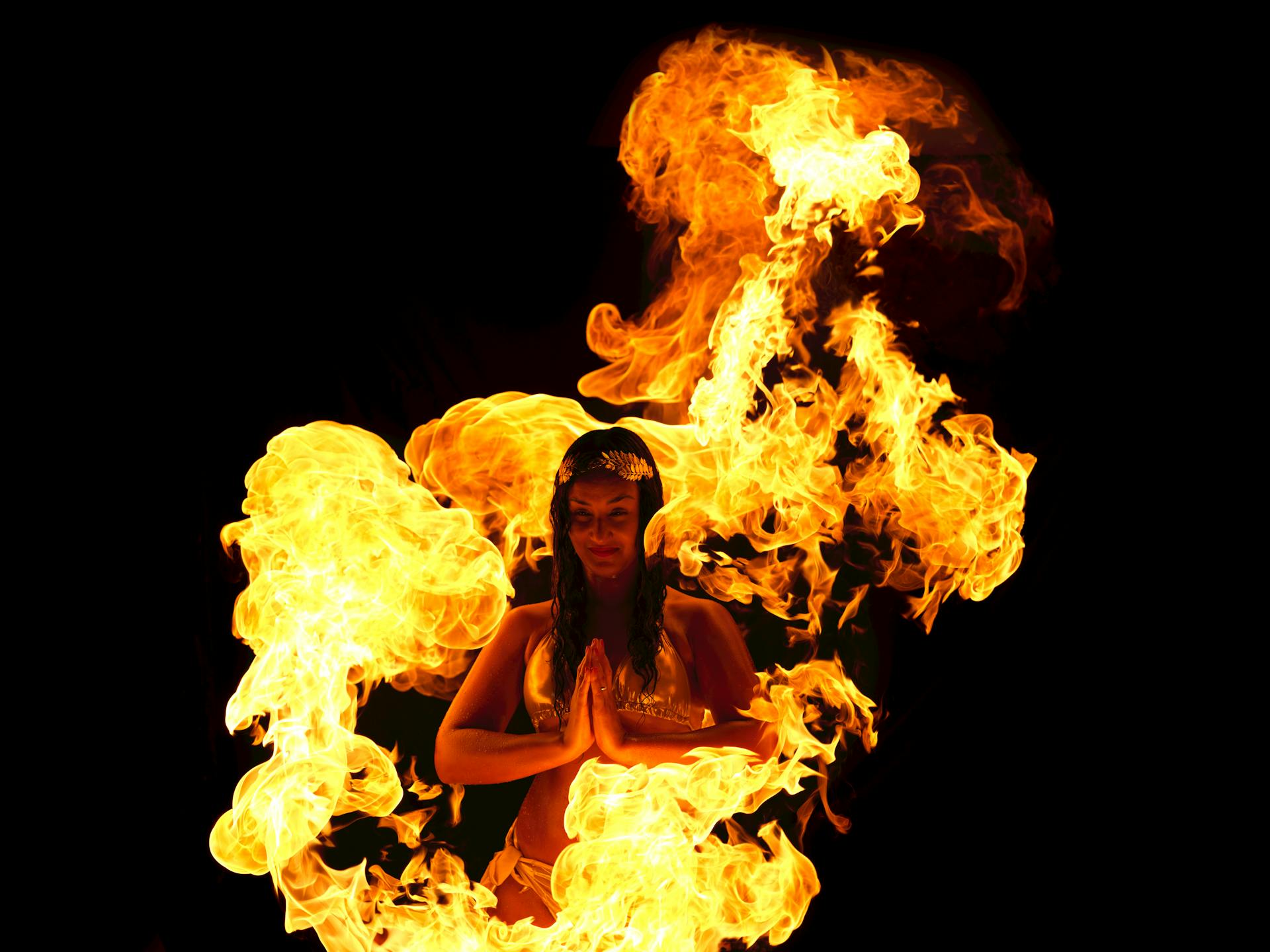 A woman performs a mesmerizing fire dance with surrounding flames on a dark background.