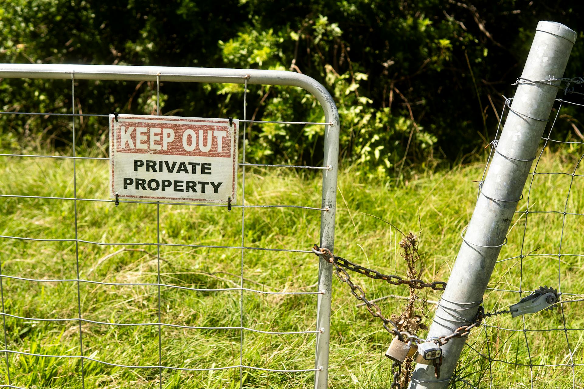 Metal fence with 'Keep Out Private Property' sign in a grassy outdoor setting.