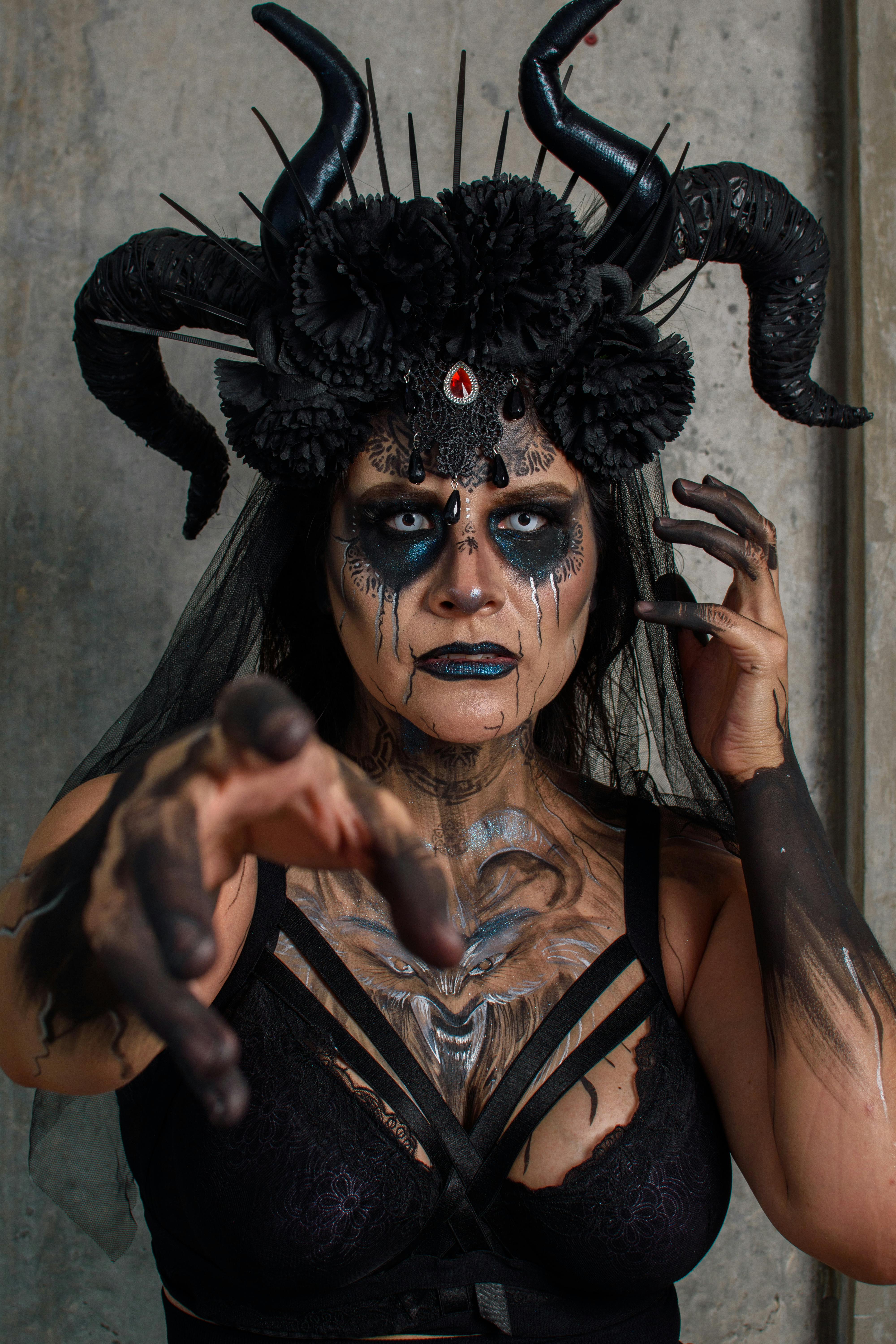 grátis Mulher mística com maquiagem escura e touca com chifres em uma arte de fantasia vívida, estendendo a mão dramaticamente. Foto profissional