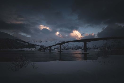 Dramatic bridge silhouette over snow-covered mountains during twilight. Perfect for winter and travel themes.