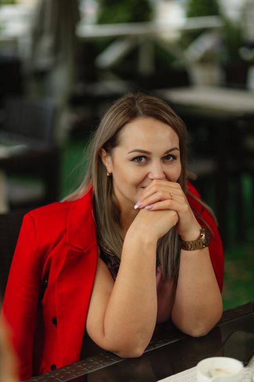 Free Happy woman in red jacket sitting at an outdoor cafe table, smiling warmly. Stock Photo