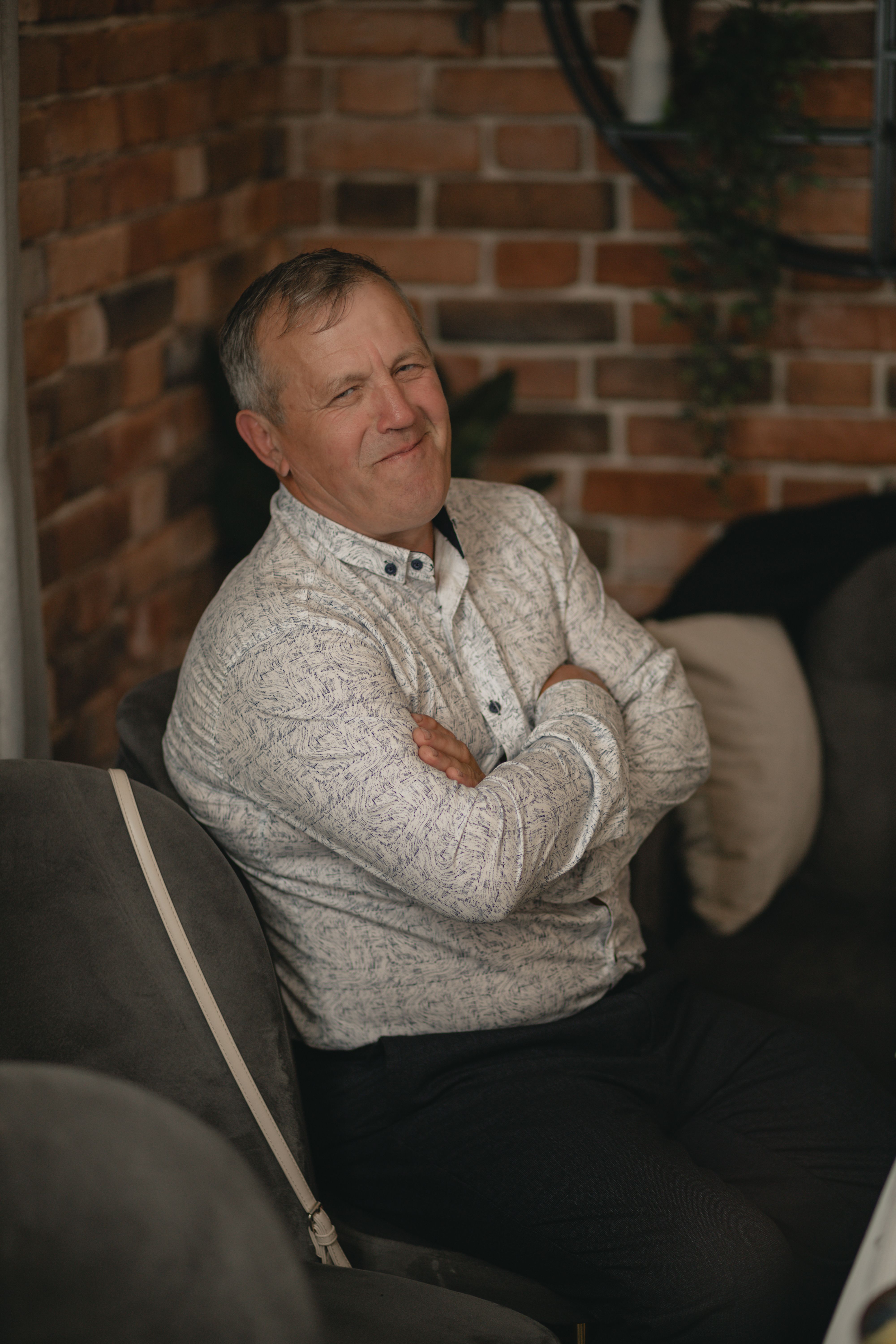 A cheerful mature man sitting and smiling inside a cozy room with brick walls.