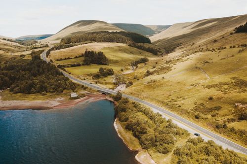 Free Aerial shot of Welsh countryside with hills, a road, and a lake, showcasing lush greenery and natural beauty. Stock Photo