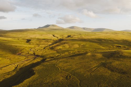 Free Stunning aerial landscape of expansive green hills and distant mountains at sunset. Stock Photo