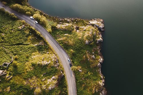 Free A stunning aerial shot of a winding road along a rocky coastline surrounded by lush greenery. Stock Photo