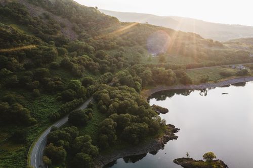 Free Stunning aerial view of a mountain landscape with a winding road and serene water reflection at sunrise. Stock Photo