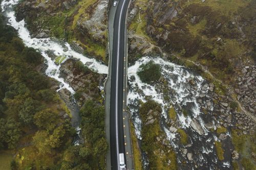 Free Drone shot of a scenic bridge crossing a vibrant river surrounded by lush greenery and rocky landscape. Stock Photo