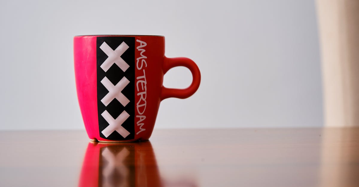 Red mug with Amsterdam's iconic XXX design on a reflective surface.
