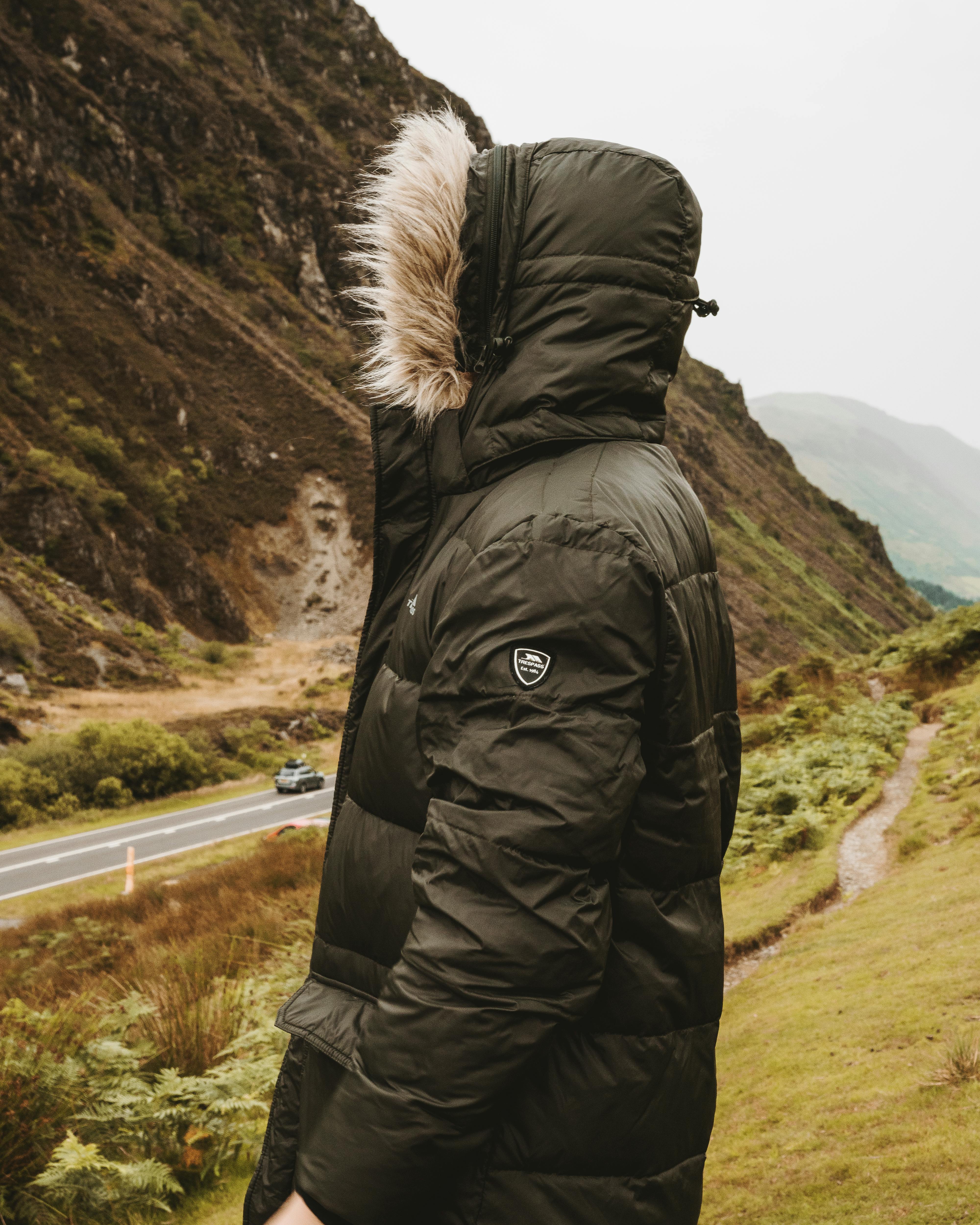 一个穿着温暖黑色夹克的人站在山路上，捕捉着大自然的美丽与旅行精神