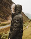 一个穿着温暖黑色夹克的人站在山路上，捕捉着大自然的美丽与旅行精神