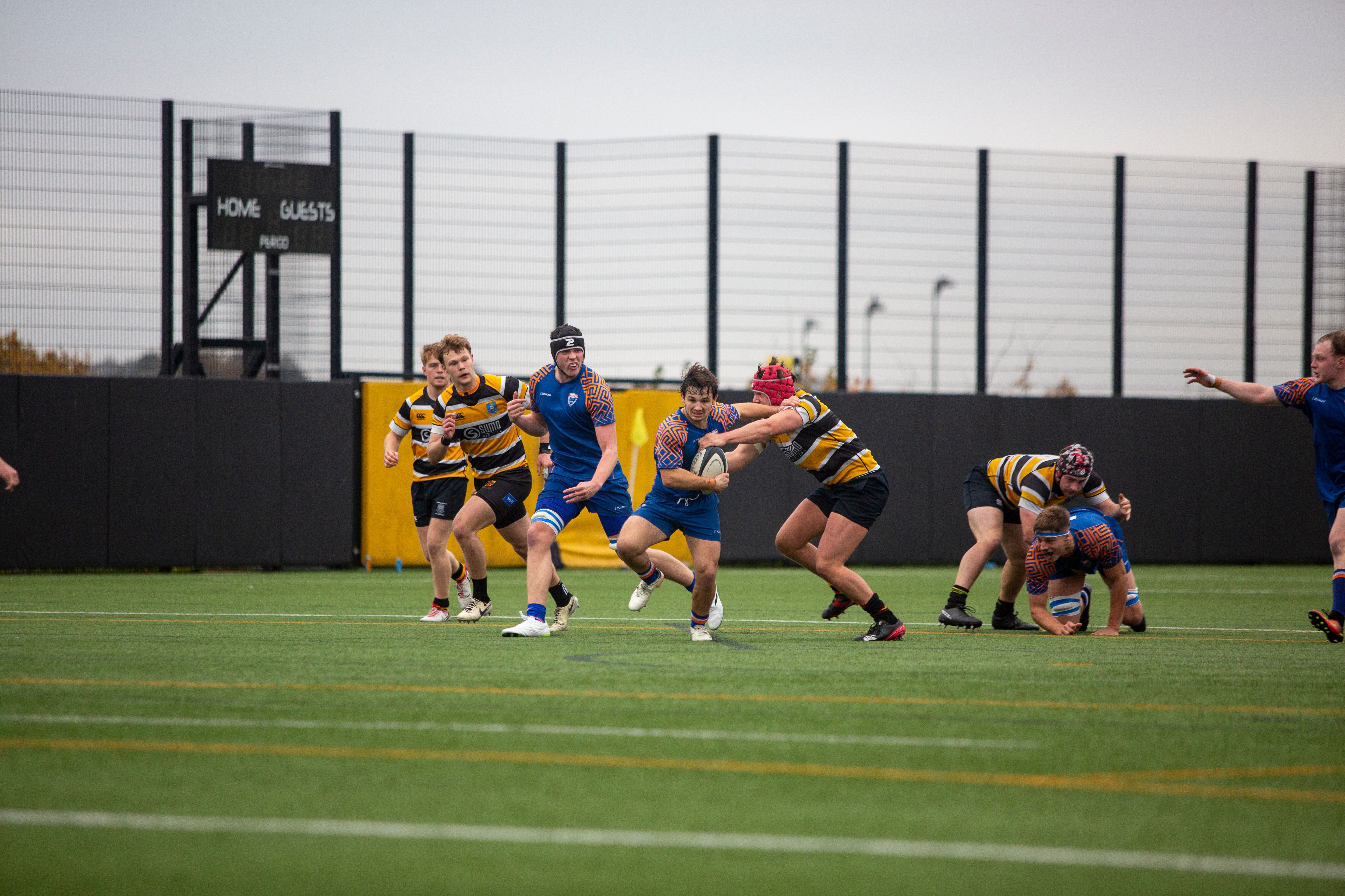 Dynamic action scene from a rugby match with players in full motion on a university field.