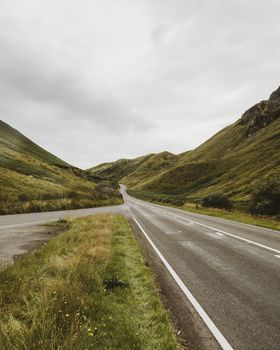 A winding road through lush green hills and an expansive rural landscape under a cloudy sky.