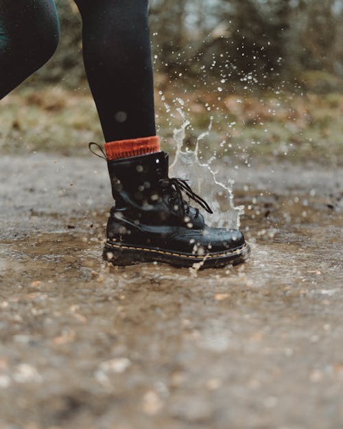 Free Water Splashing From A Person In Black Workers Boots Stepping On Wet Pavement Stock Photo