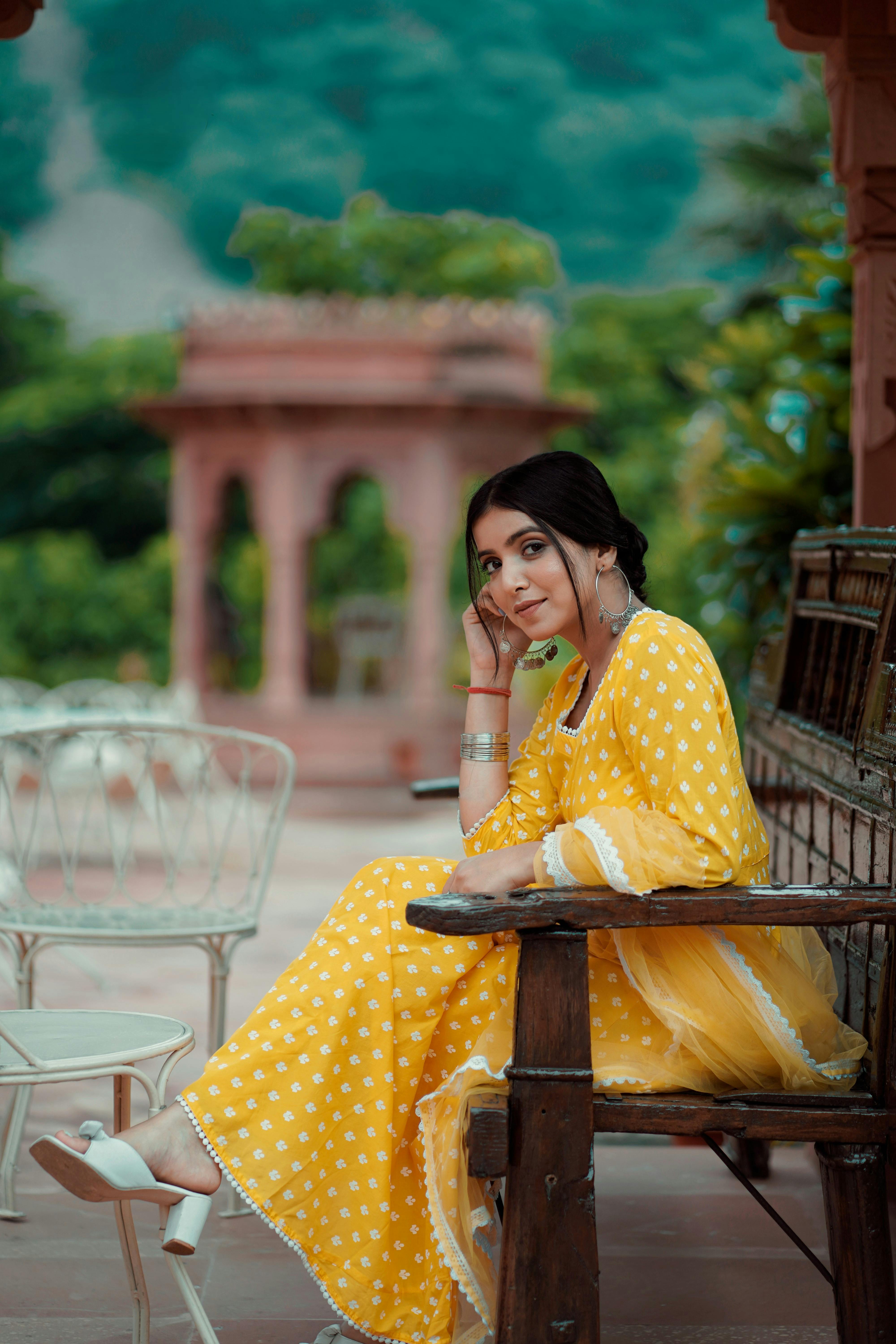 Woman in a yellow polka dot dress sits gracefully in an outdoor setting.