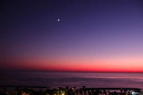 Free Spectacular sunset over ocean with crescent moon and vivid colors in the sky. Stock Photo
