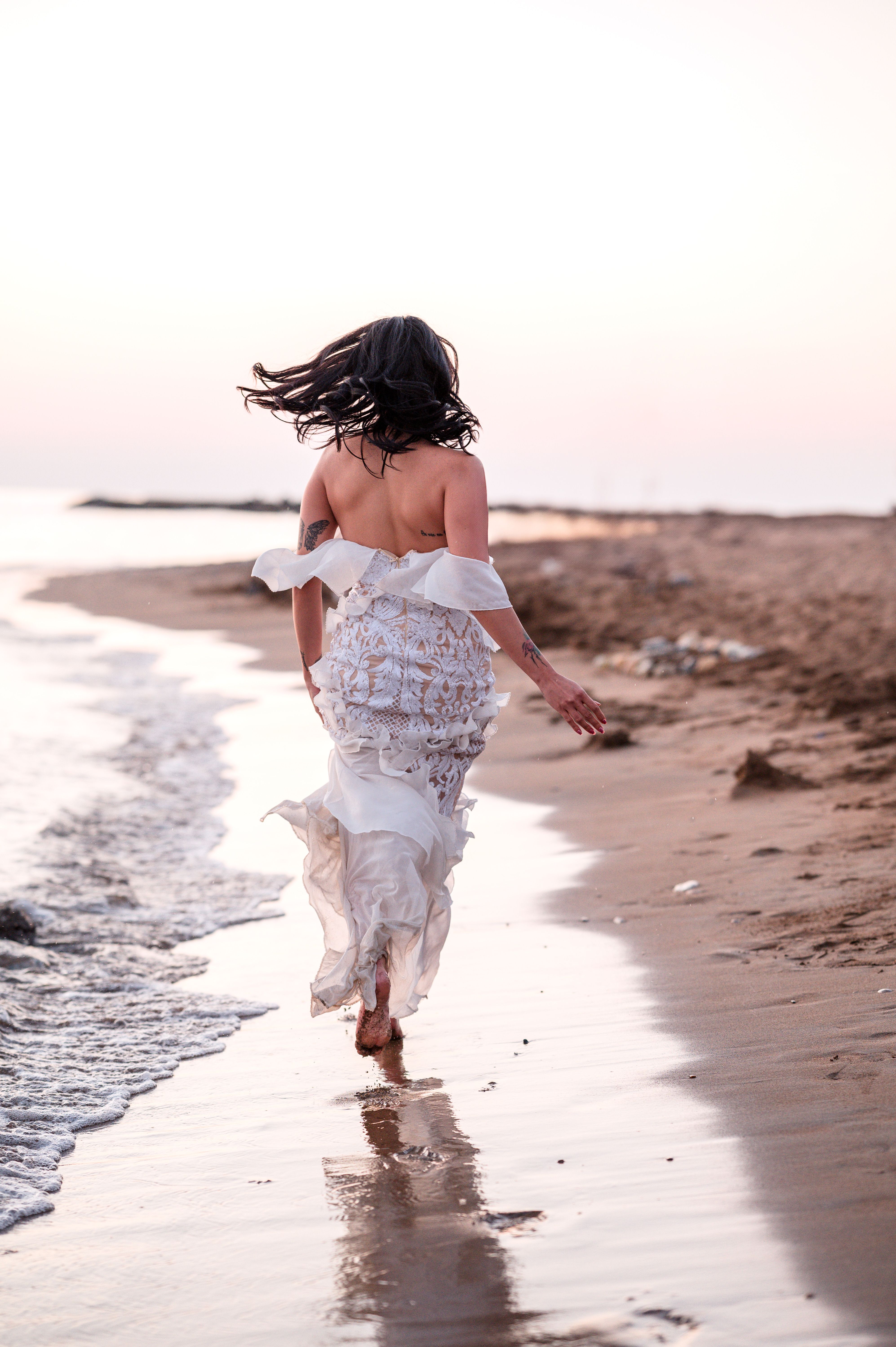 Woman in flowing dress running on beach at sunset · Free Stock Photo