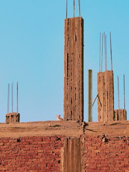 A construction site with exposed brickwork against a clear blue sky, featuring visible support columns.