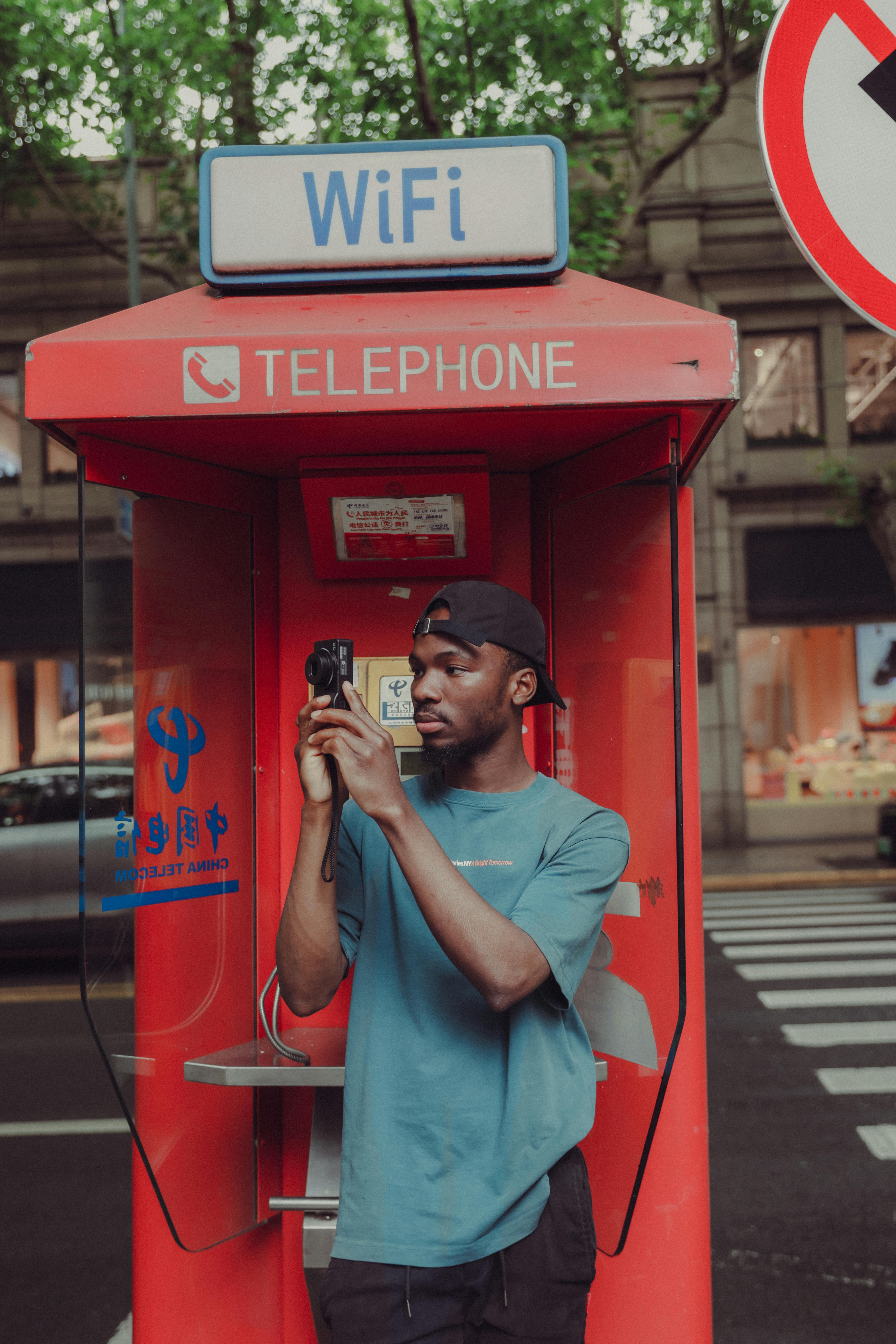 A casual scene of a man capturing a moment using a camera at a red telephone booth featuring a WiFi sign.