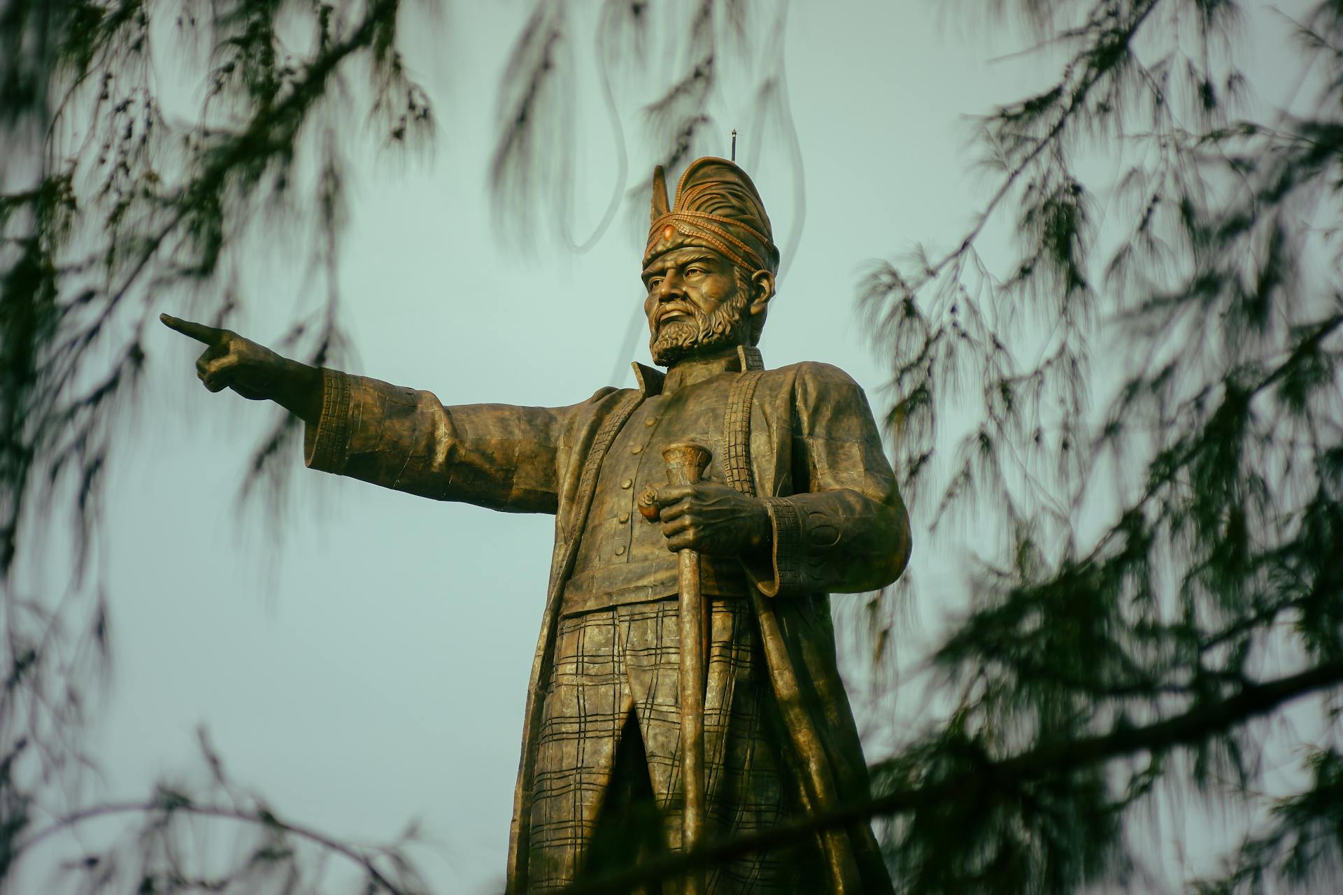 Bronze statue of a historical figure surrounded by tree branches.