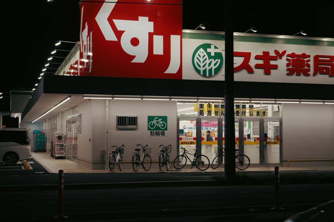 Sugi Pharmacy storefront in Japan at dusk with illuminated signage and bicycles outside