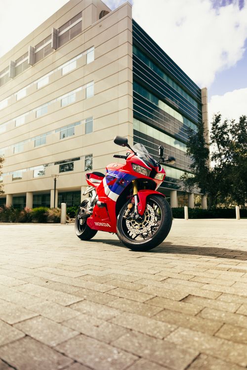 Free A vibrant red and blue motorcycle parked in front of a modern building on a sunny day. Stock Photo