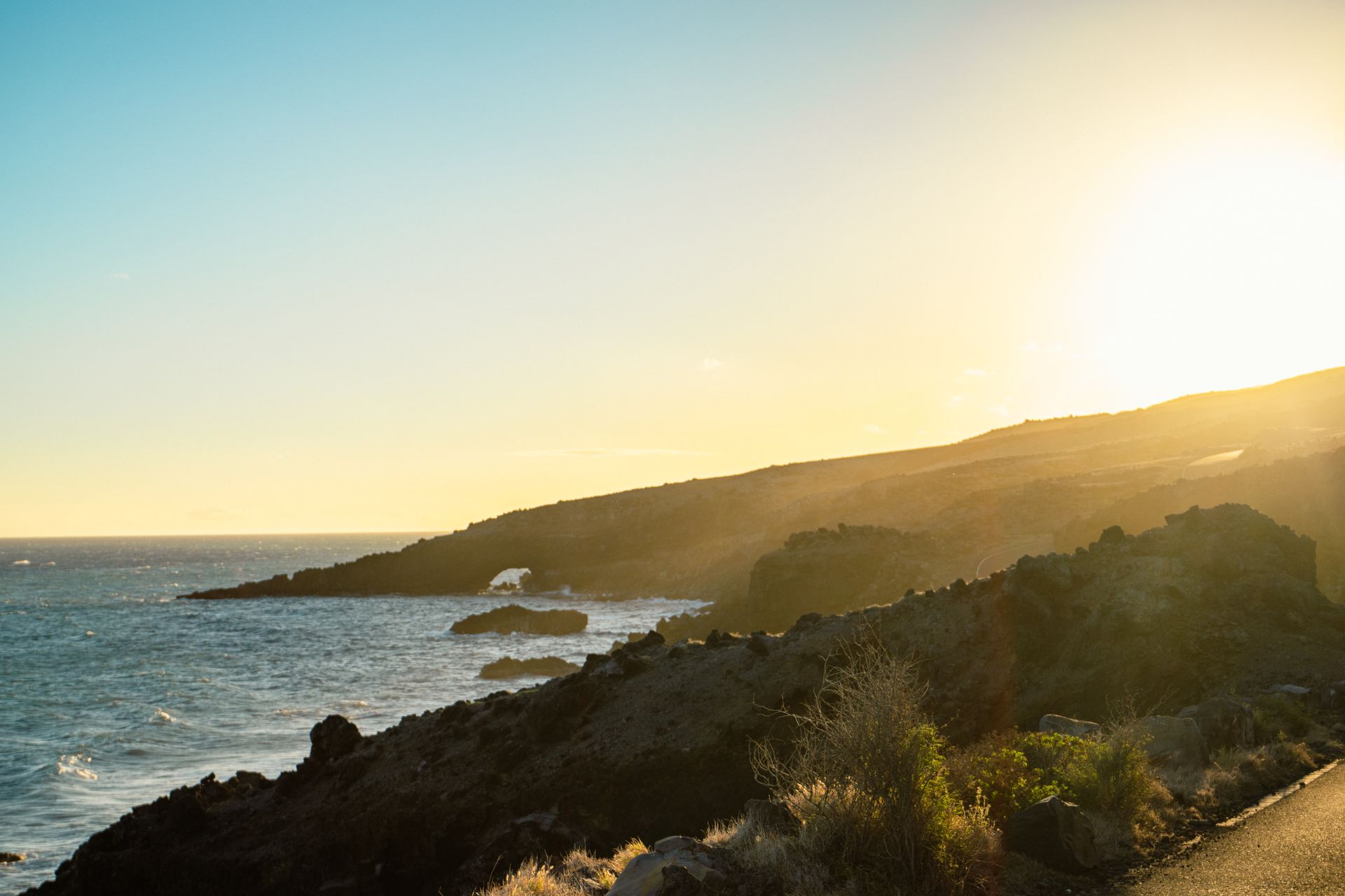 Beautiful golden sunset over a rugged Hawaiian coastline with ocean waves crashing.