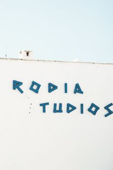Aegean-style white wall with blue letters under clear sky in Naxos, Greece.