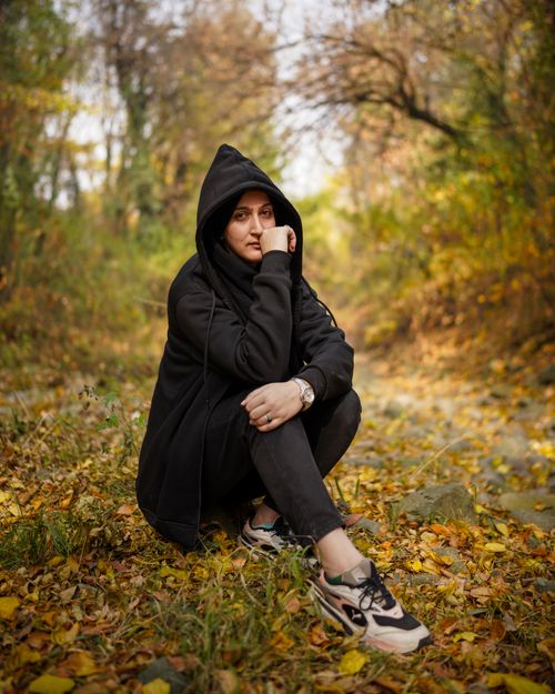 Free A woman in a hoodie sits on fallen leaves in a vibrant autumn forest, conveying a contemplative mood. Stock Photo