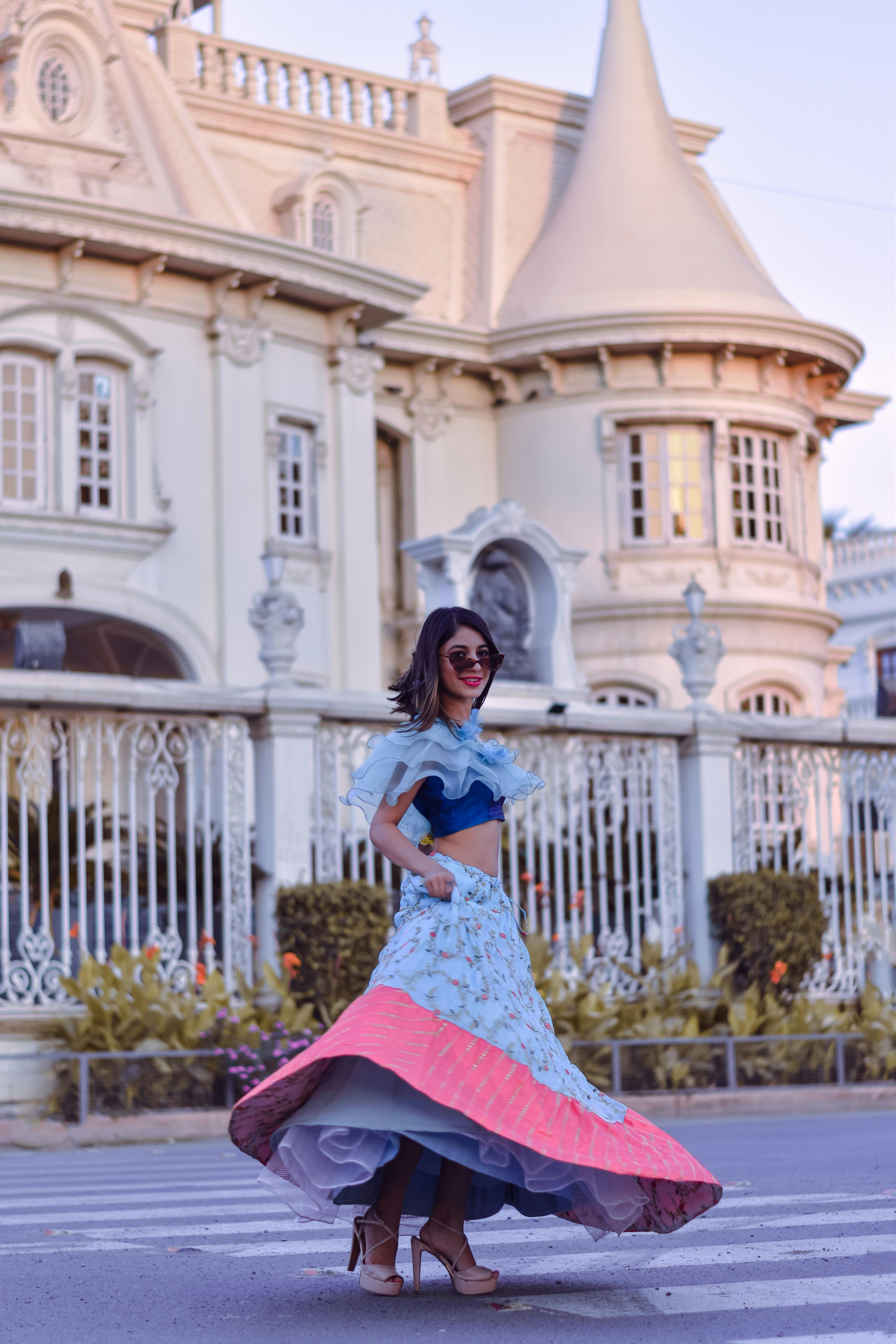 一位身着彩色连衣裙的时尚女子，在阳光明媚的历史建筑旁优雅地摆着姿势